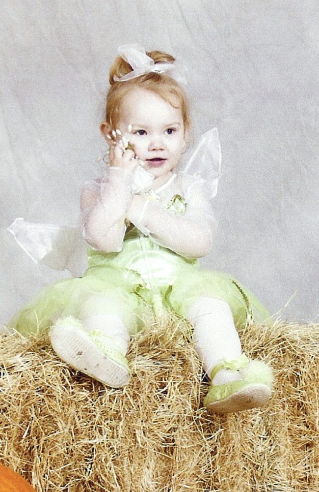 Toddler Marissa in a Tinker Bell costume, sitting on a hay bale
